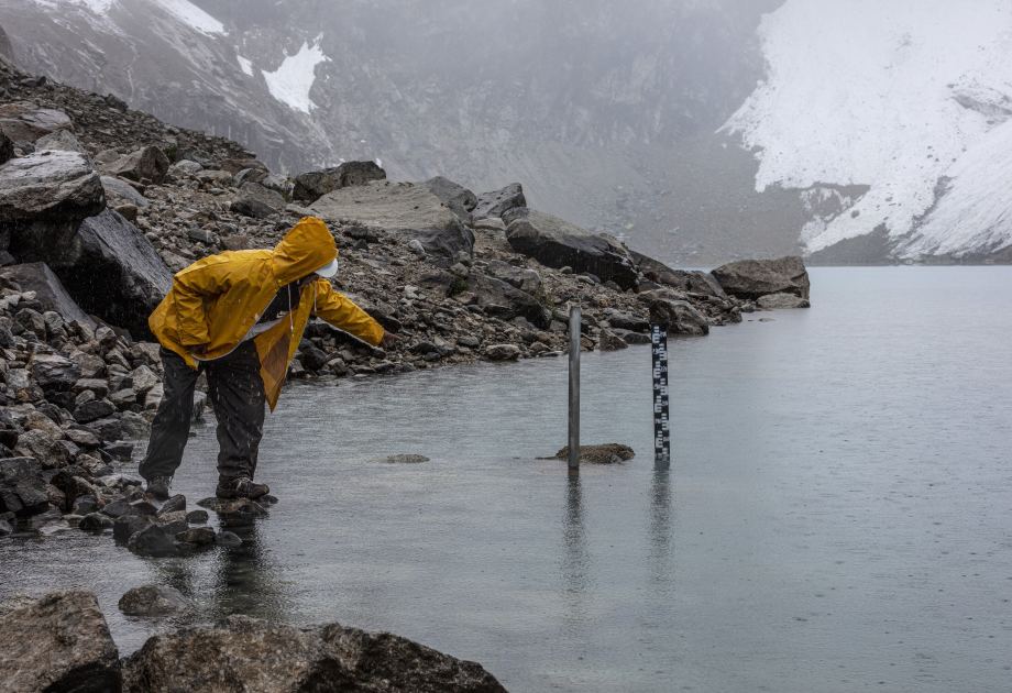 Gletscherwächter misst den Wasserstand des Sees Ein Gletscherseewächter in einer gelben Regenjacke misst den Wasserstand der Lagune