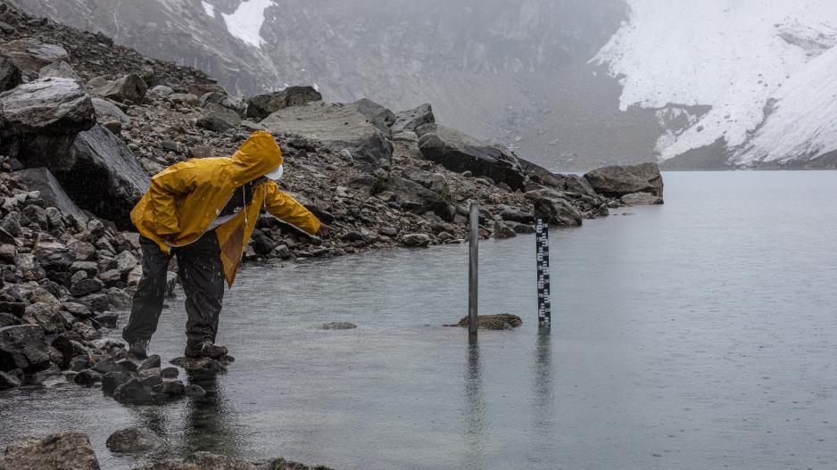 A glacier lake guard in a yellow rain jacket measures the water level of the lagoon